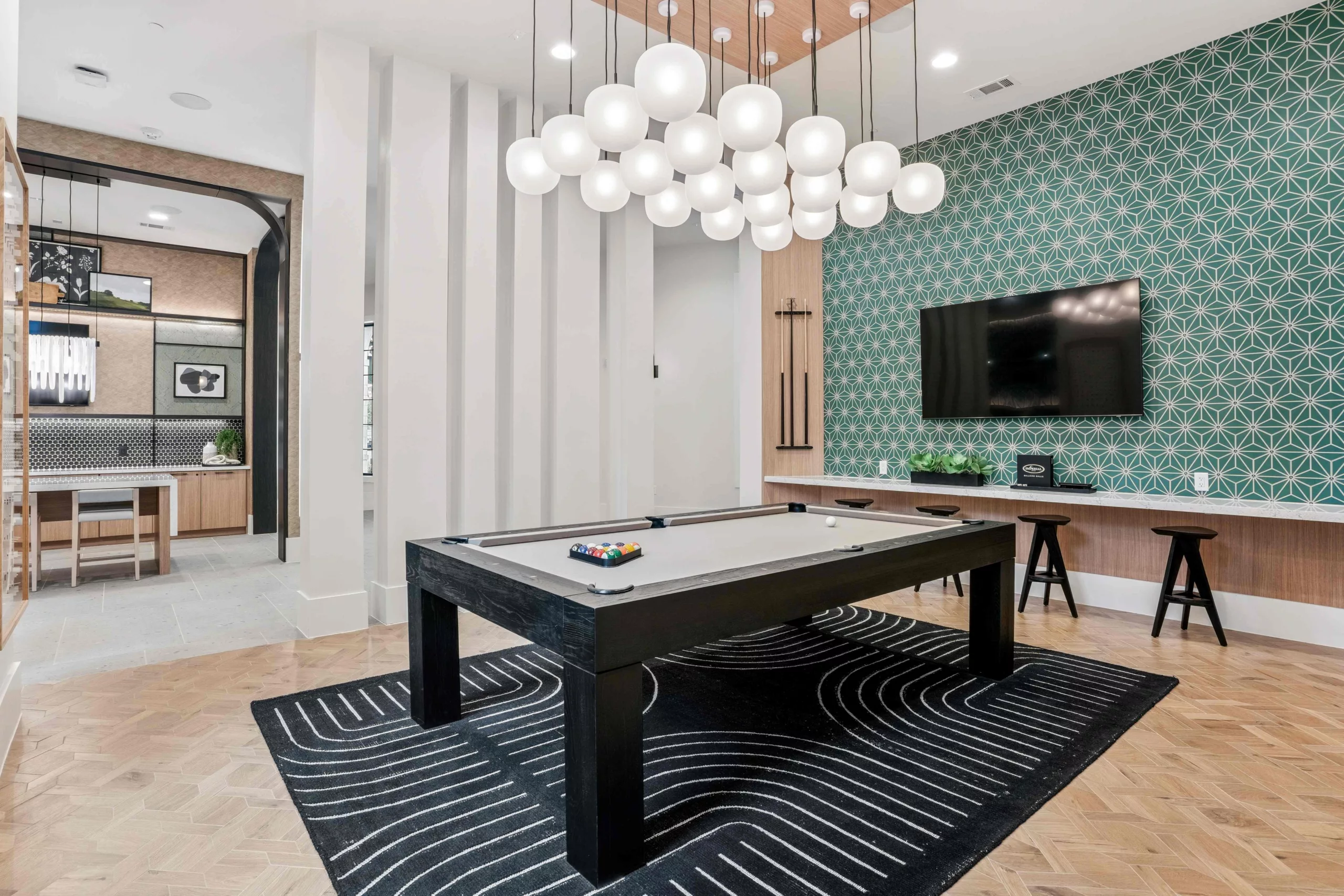 Game billiards lounge with pool table, bar seating, geometric wallpaper, and globe chandelier.