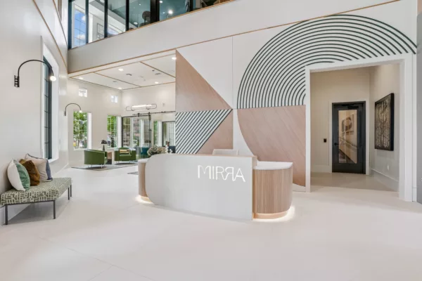 Grand lobby with white reception desk and branded geometric wall design. Lounge seating available in front of the leasing center.
