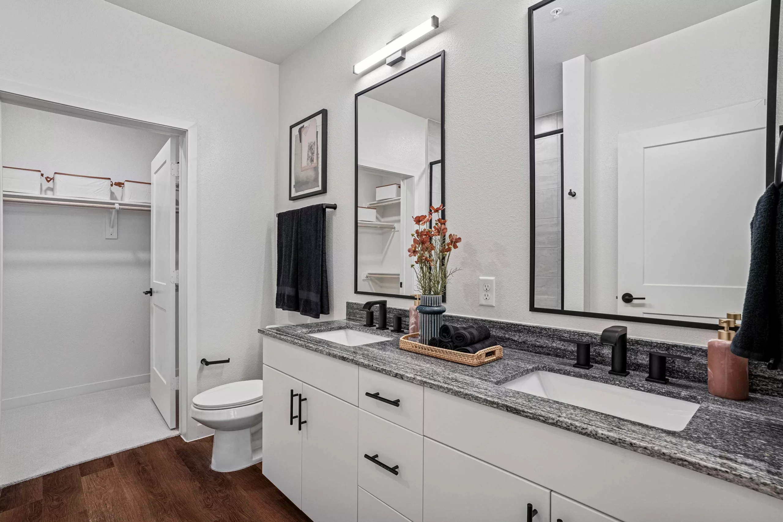 Bathroom with double vanity, granite countertop, black fixtures, and a door opened to a closet.