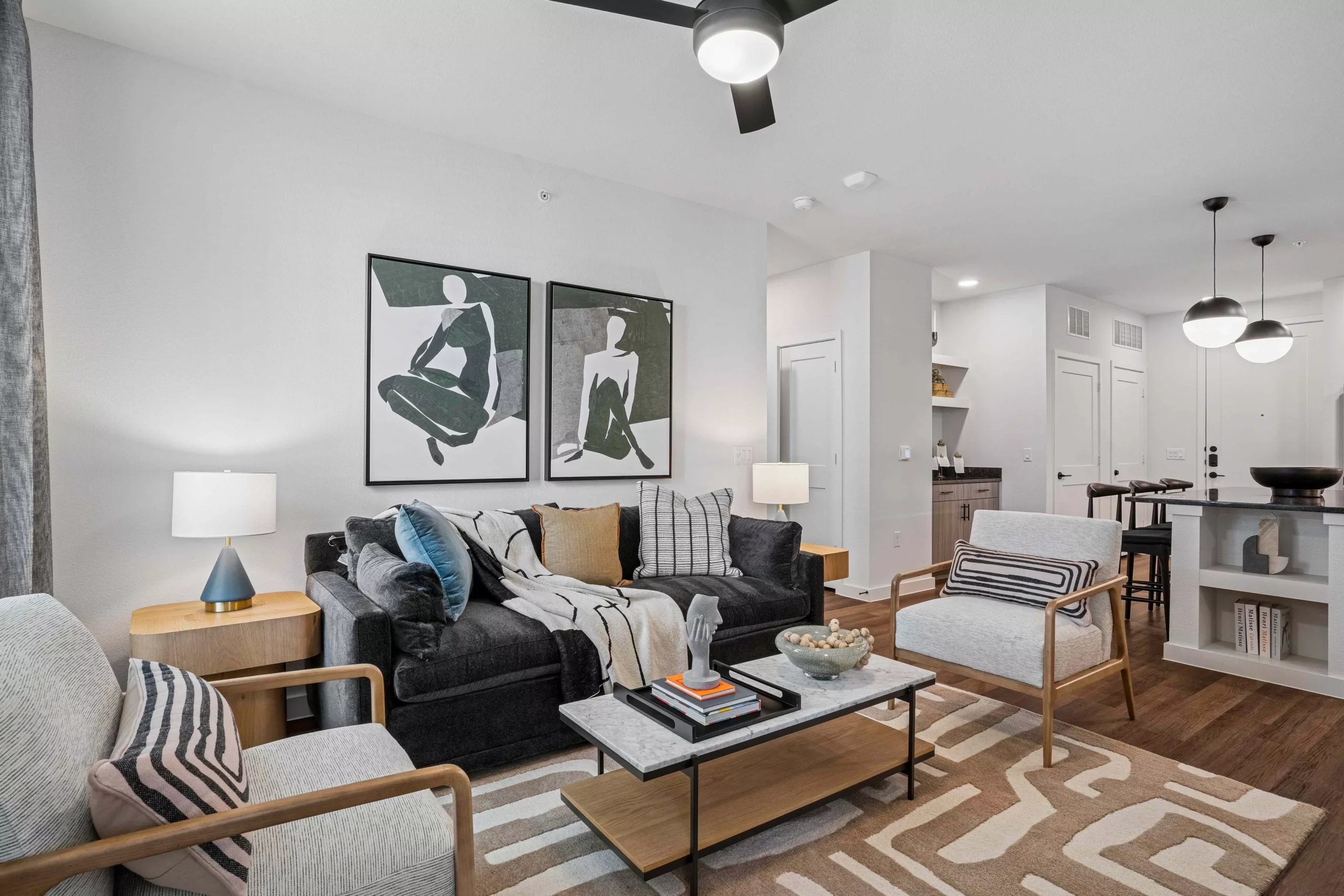 Modern living room with dark sofa, light chairs, and wood floors and artwork above couch.