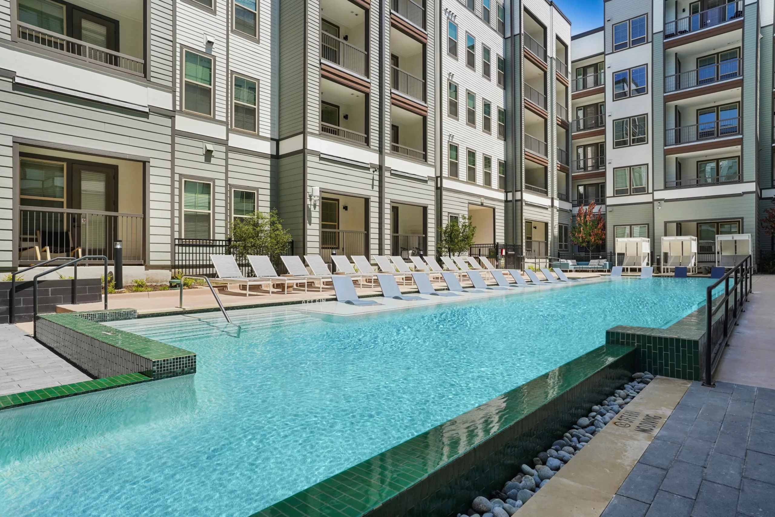 Outdoor pool with lounge chairs and multi-story building in the background.