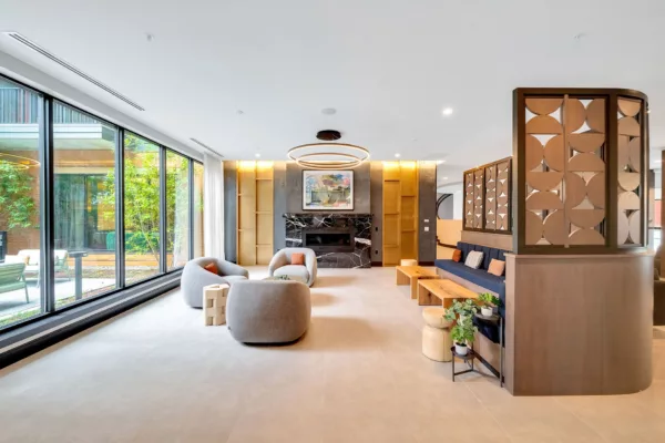 Modern lounge with fireplace, seating, and large windows overlooking greenery.