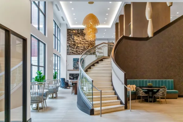 Grand lobby with curved staircase, seating areas, and modern chandelier.