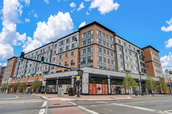 Multi-story building with brick and gray siding, street-level retail, and blue sky.