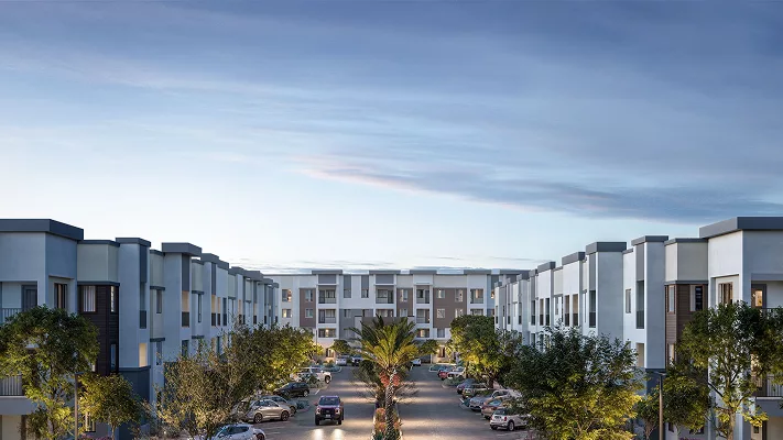 Modern apartment complex with palm trees and parked cars under a blue sky.