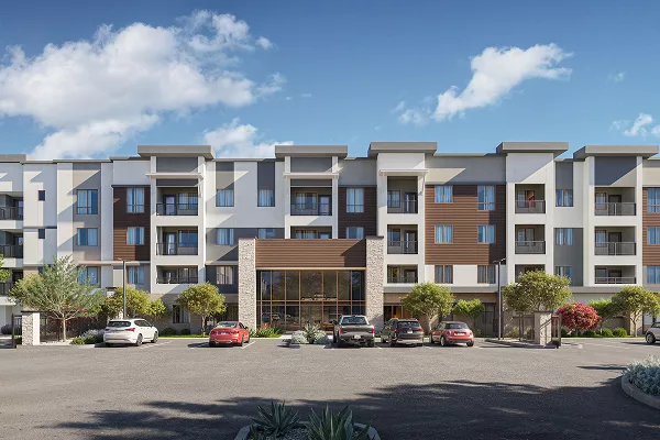 Modern four-story apartment building with cars parked in front under a blue sky.