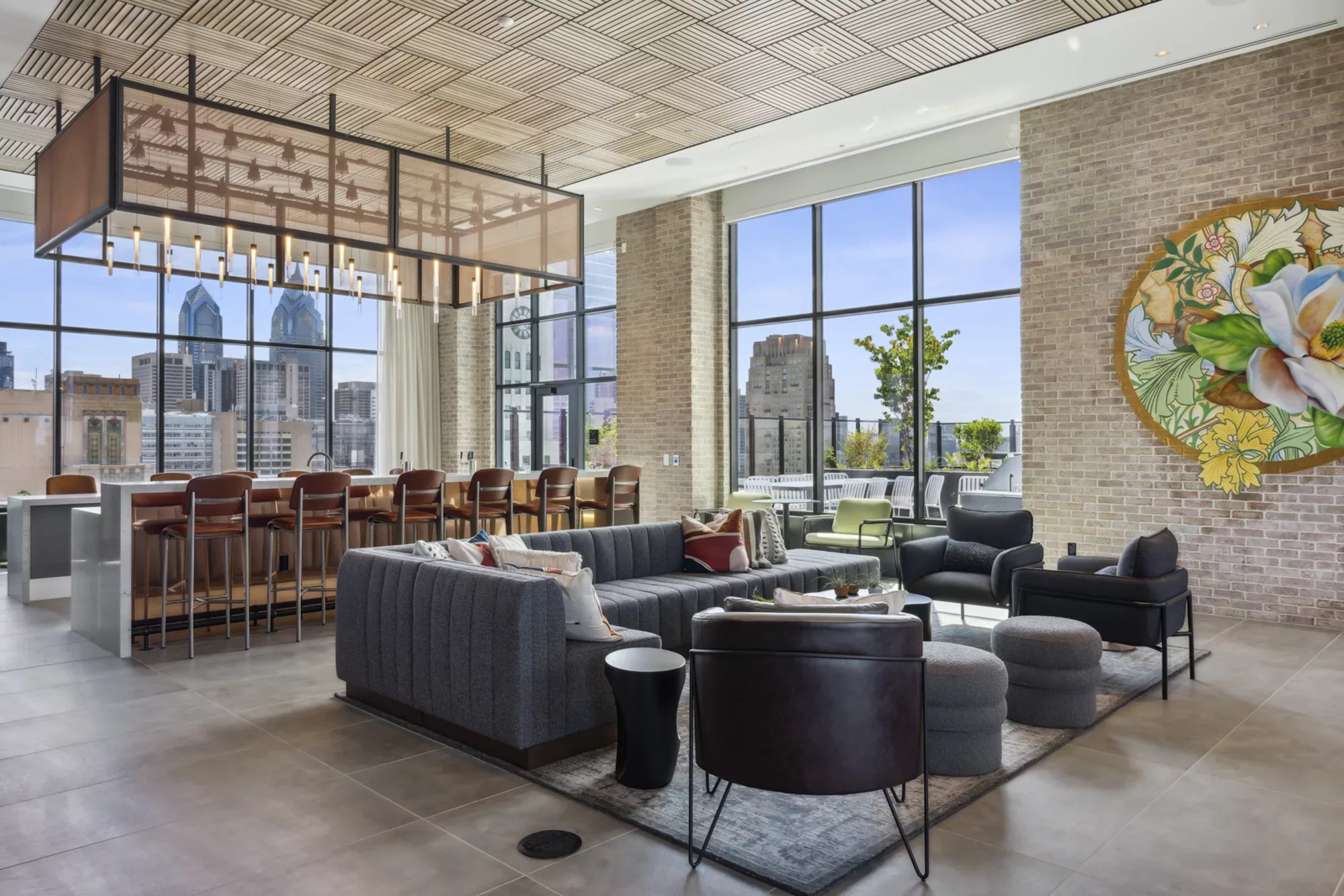 Rooftop lounge with bar, seating area, brick wall with mural, and views of the city skyline